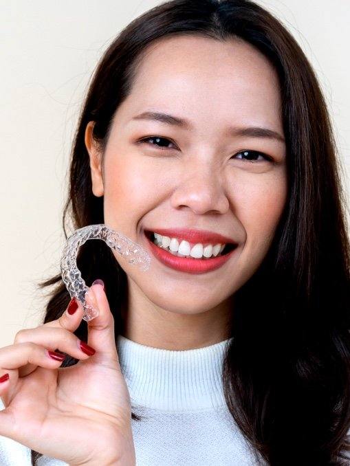 Woman holding a clear aligner tray in front of her smile