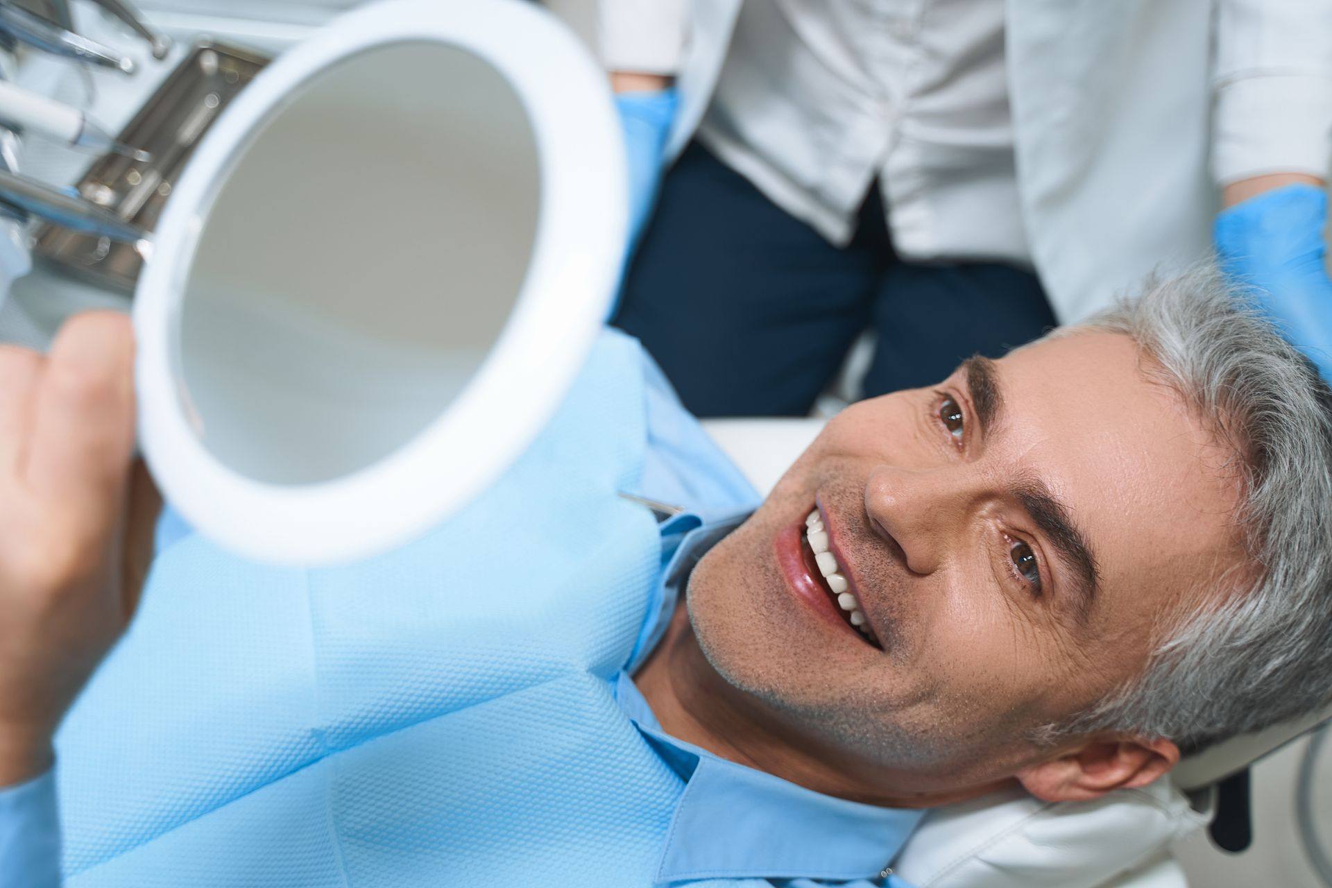 Smiling man reclined in a dental chair checking his teeth in a hand mirror