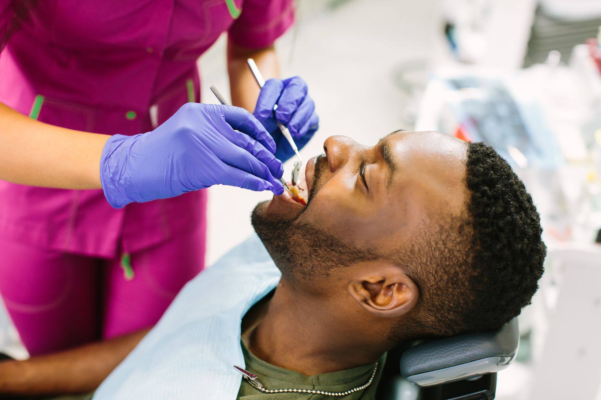 Dentist in pink scrubs examining a smiling man's teeth