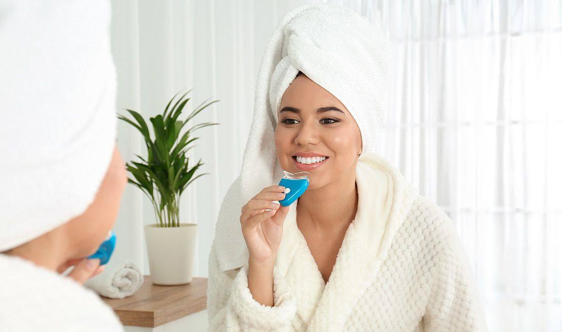 Woman in a bathrobe placing a whitening tray at home
