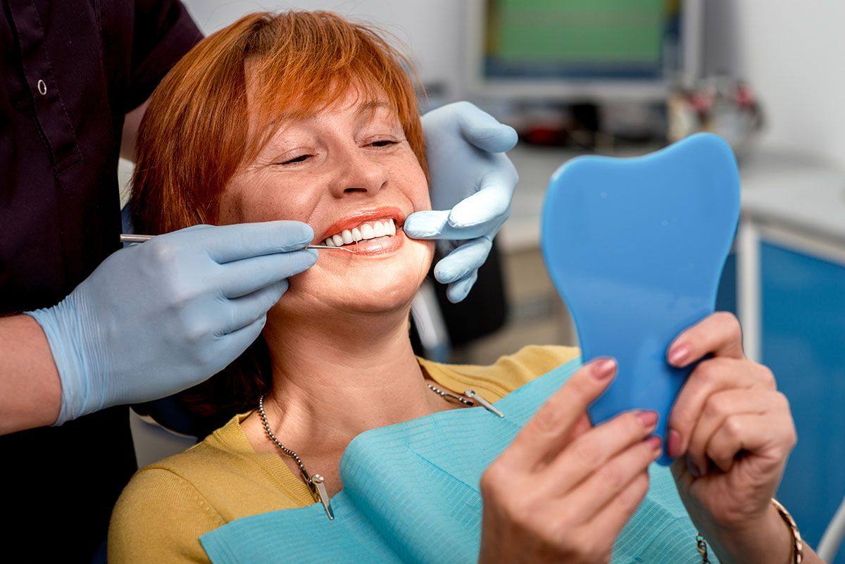 Smiling woman holding a tooth-shaped mirror during a dental visit
